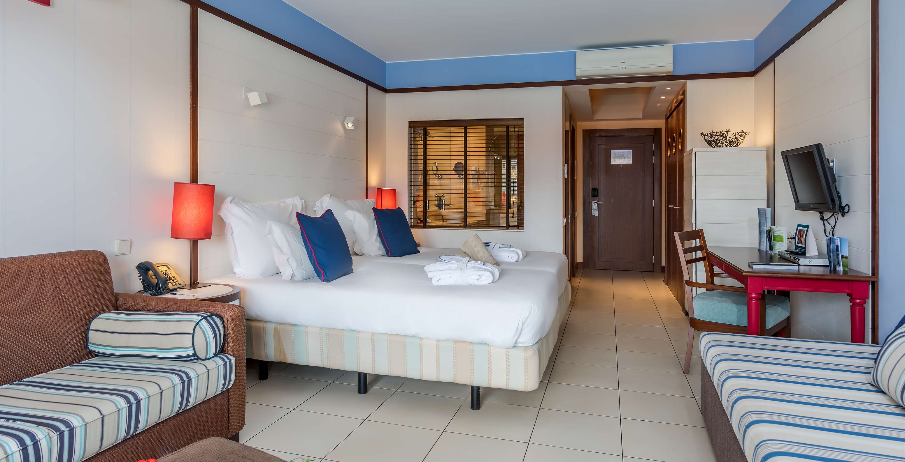 De Familiekamer van Pestana Porto Santo All Inclusive heeft twee bedden twee banken een bureau en een televisie