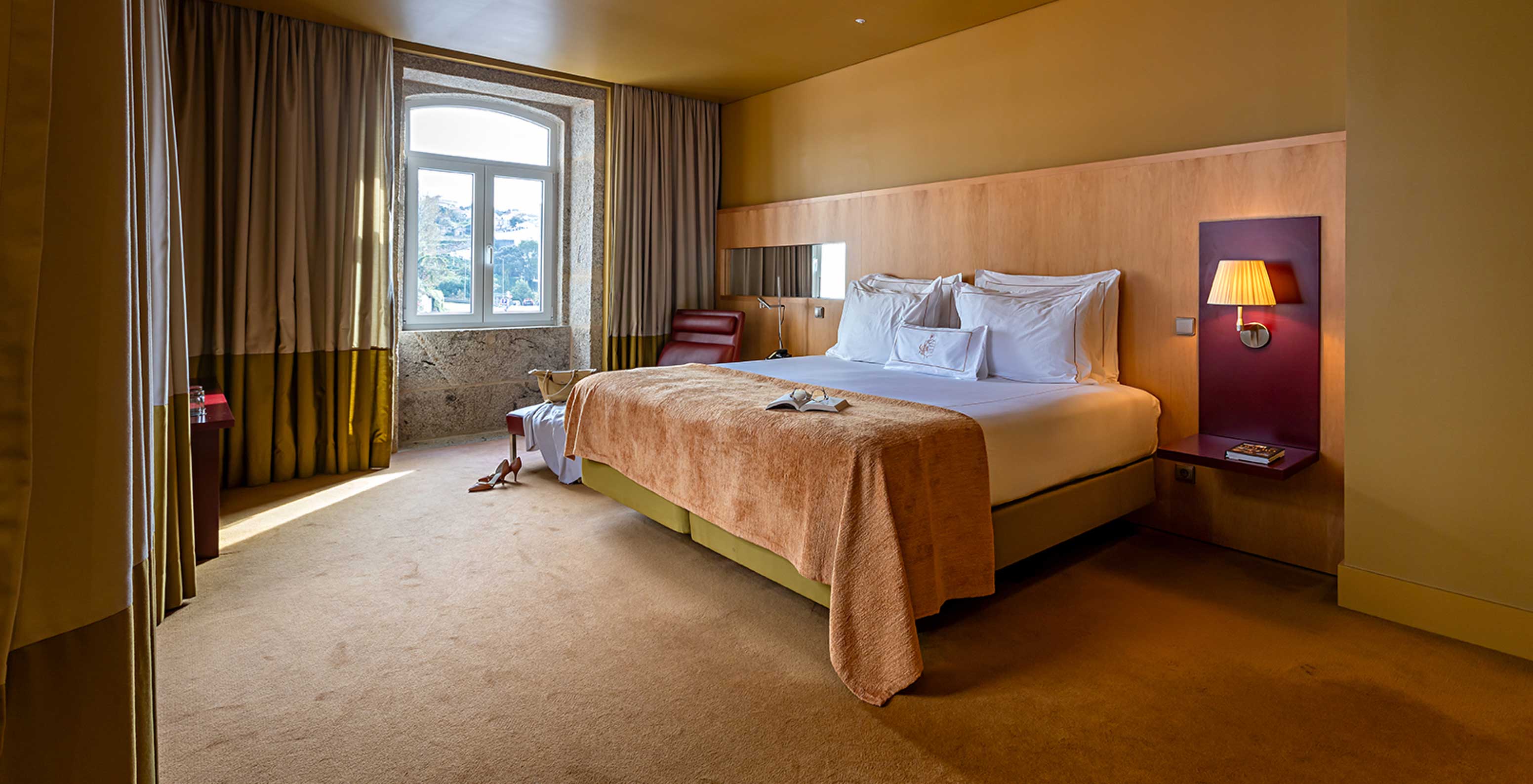 De Junior Suite heeft een tweepersoonsbed met beige deken en een stenen raam met uitzicht op de rivier