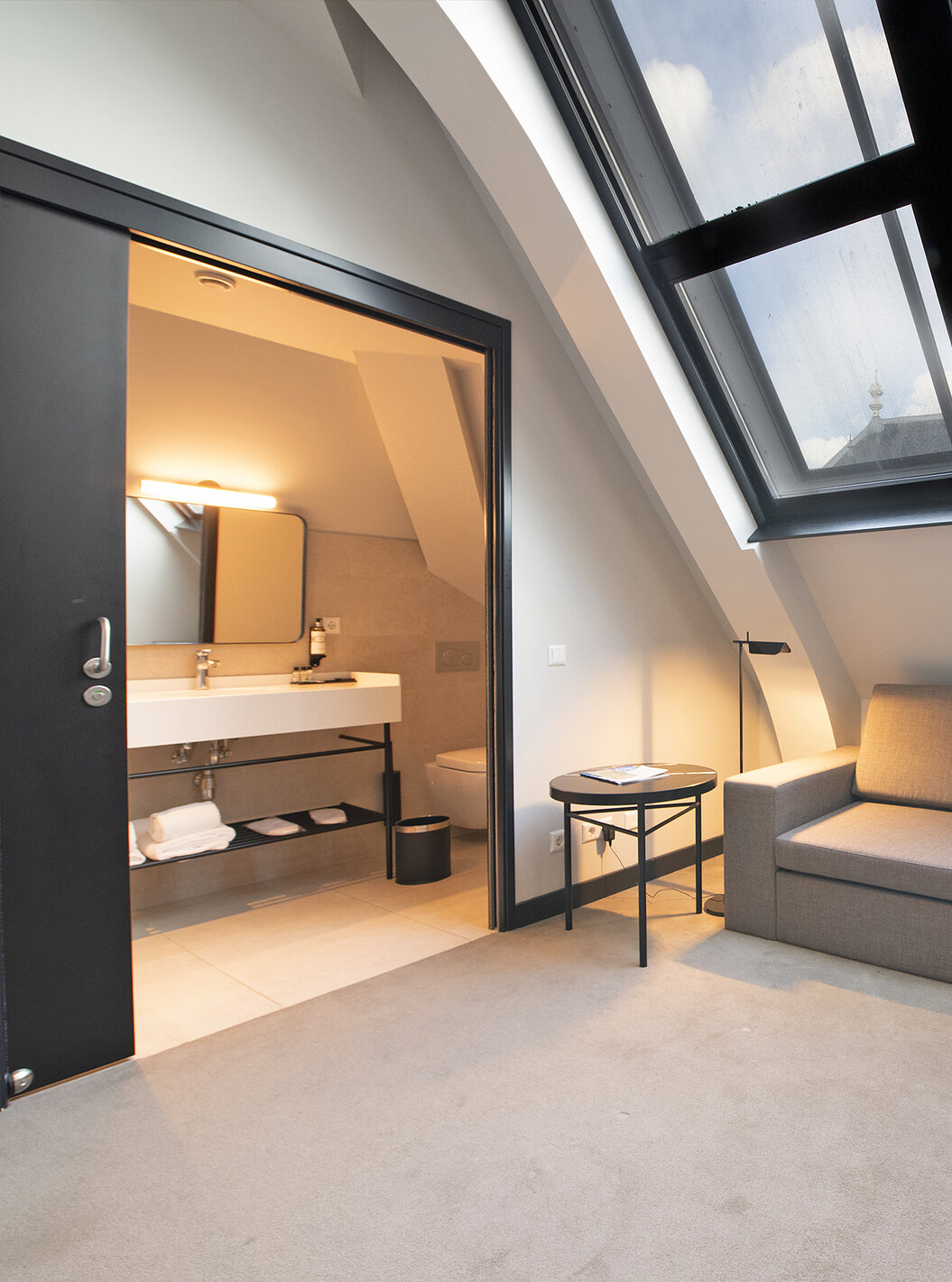 Loft kamer Pestana Amsterdam Riverside heeft grijze bank en badkamer met wastafel en spiegel