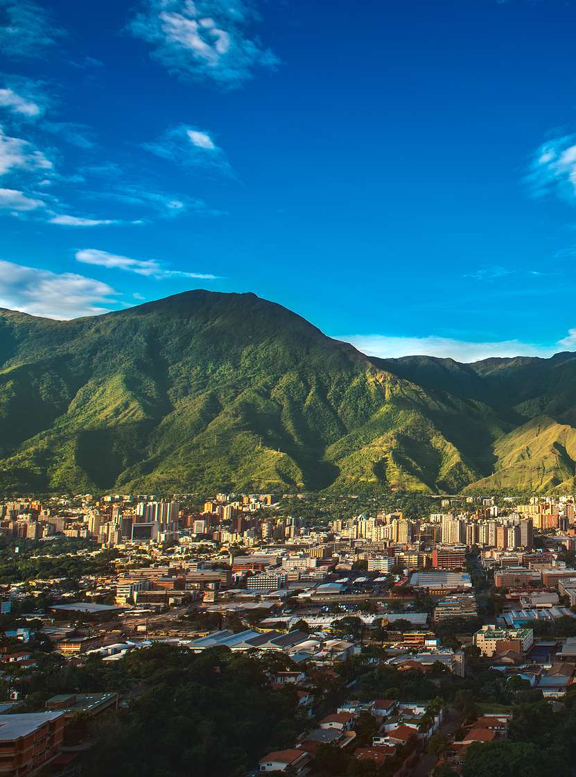 Luchtfoto van de stad Caracas met hoge gebouwen, in contrast met de bergachtige natuur en de blauwe lucht