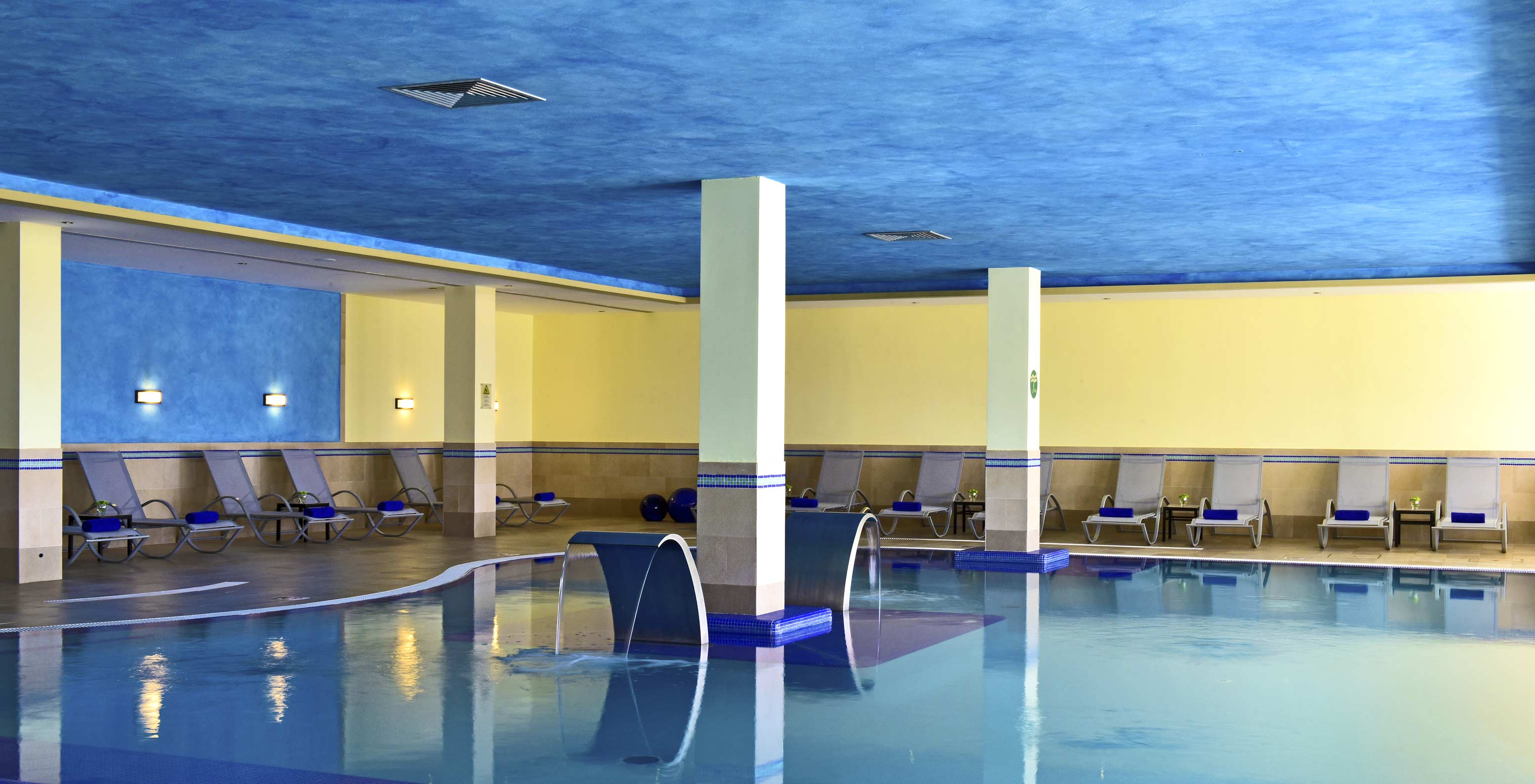 Piscina interior do Pestana Viking, com paredes em tons de azul, amarelo e ambiente calmo, com várias espreguiçadeiras
