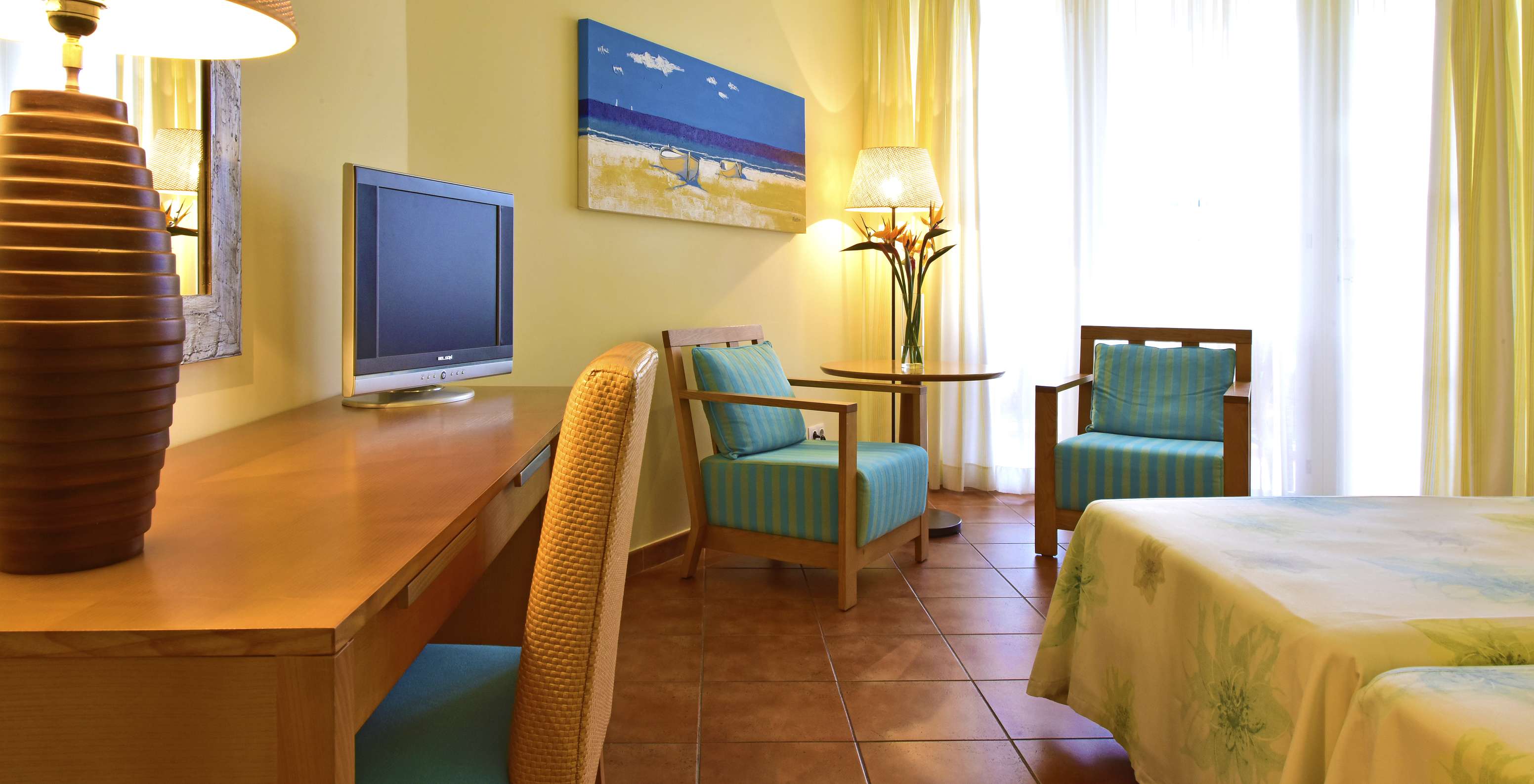 O quarto Deluxe Superior Vista Mar do Pestana Viking conta com televisão, duas cadeiras com mesa de centro, e uma secretária