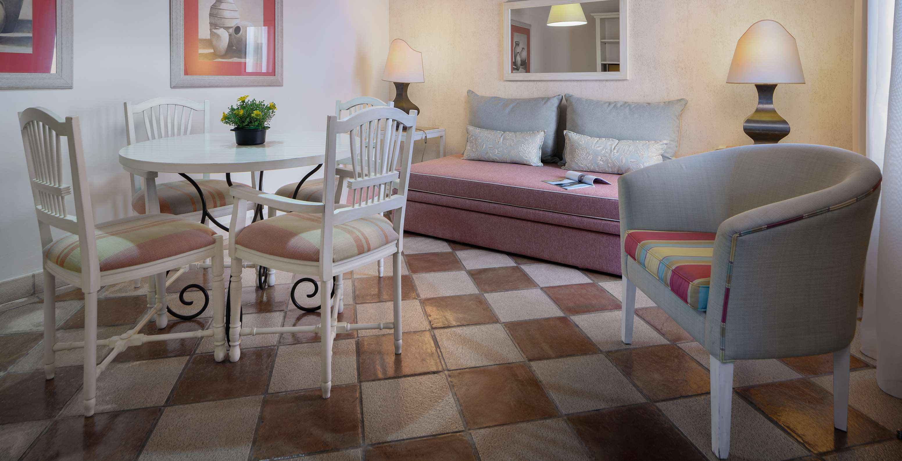 A Suite Vista Jardim do Pestana Vila Sol - Vilamoura tem uma sala com um sofá, uma mesa, cadeiras e um espelho na parede