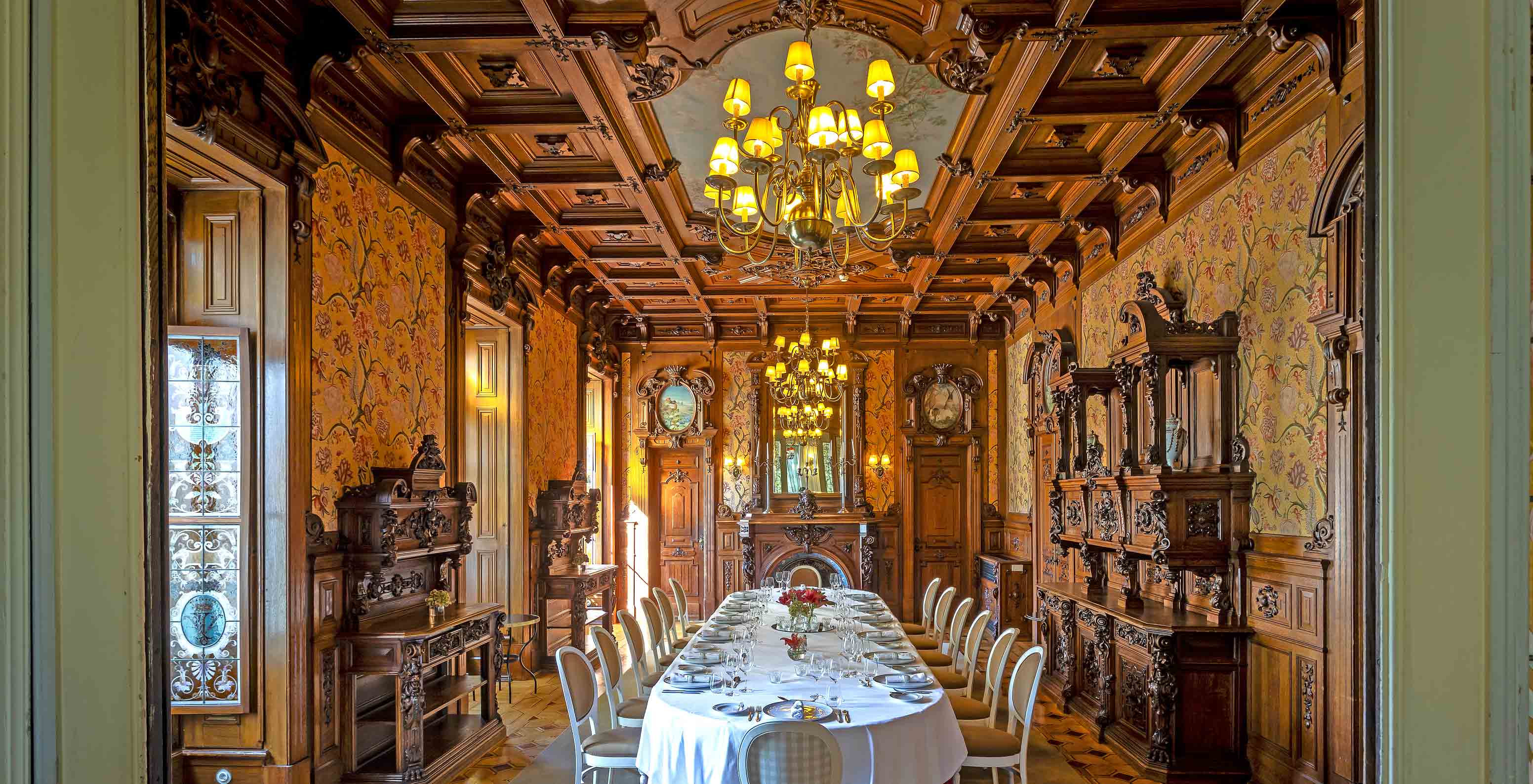 O Pestana Palace Lisboa tem uma sala de jantar privada com um teto em madeira com três candelabros e uma mesa oval