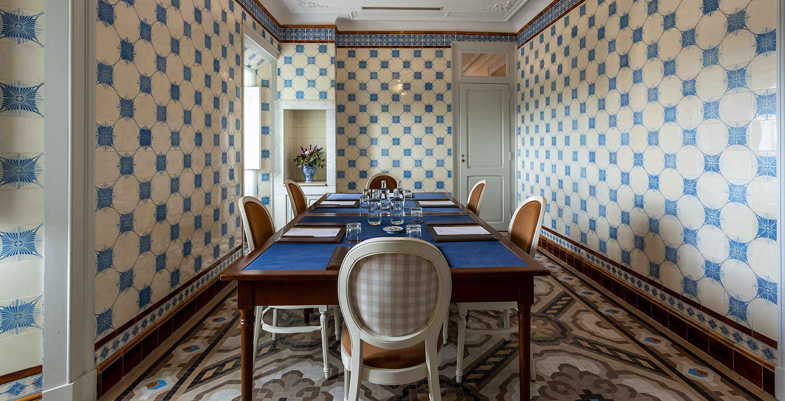 O Pestana Palace Lisboa tem uma sala de reuniões com azuleijos azuis e brancos e uma mesa rodeada de cadeiras brancas