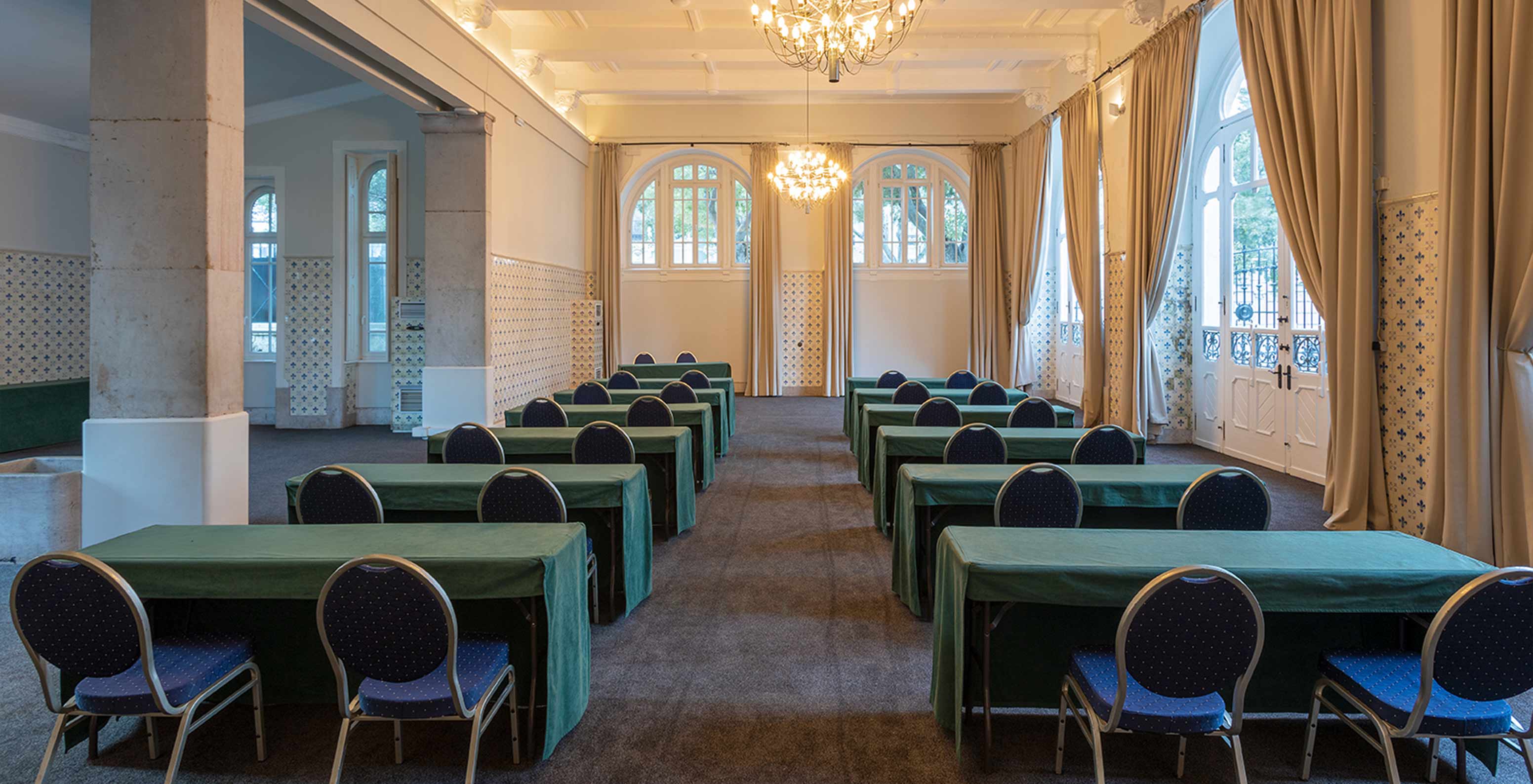 O Pestana Palace Lisboa tem uma sala de reuniões com mesas verdes e cadeiras azuis, e várias janelas 