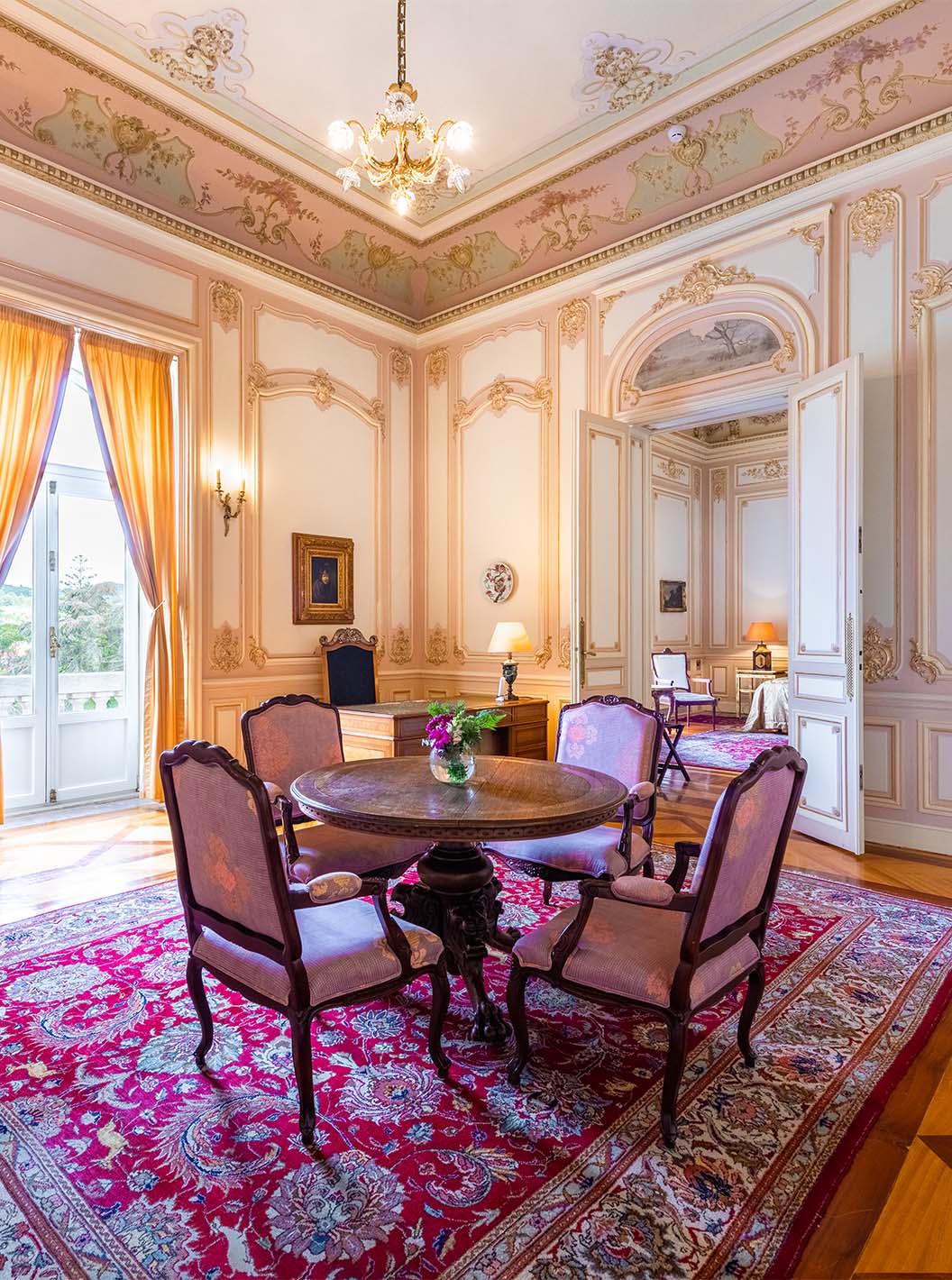 A Suite D. Carlos do Pestana Palace Lisboa tem um salão grande e luxuoso com uma janela e mesa para refeições