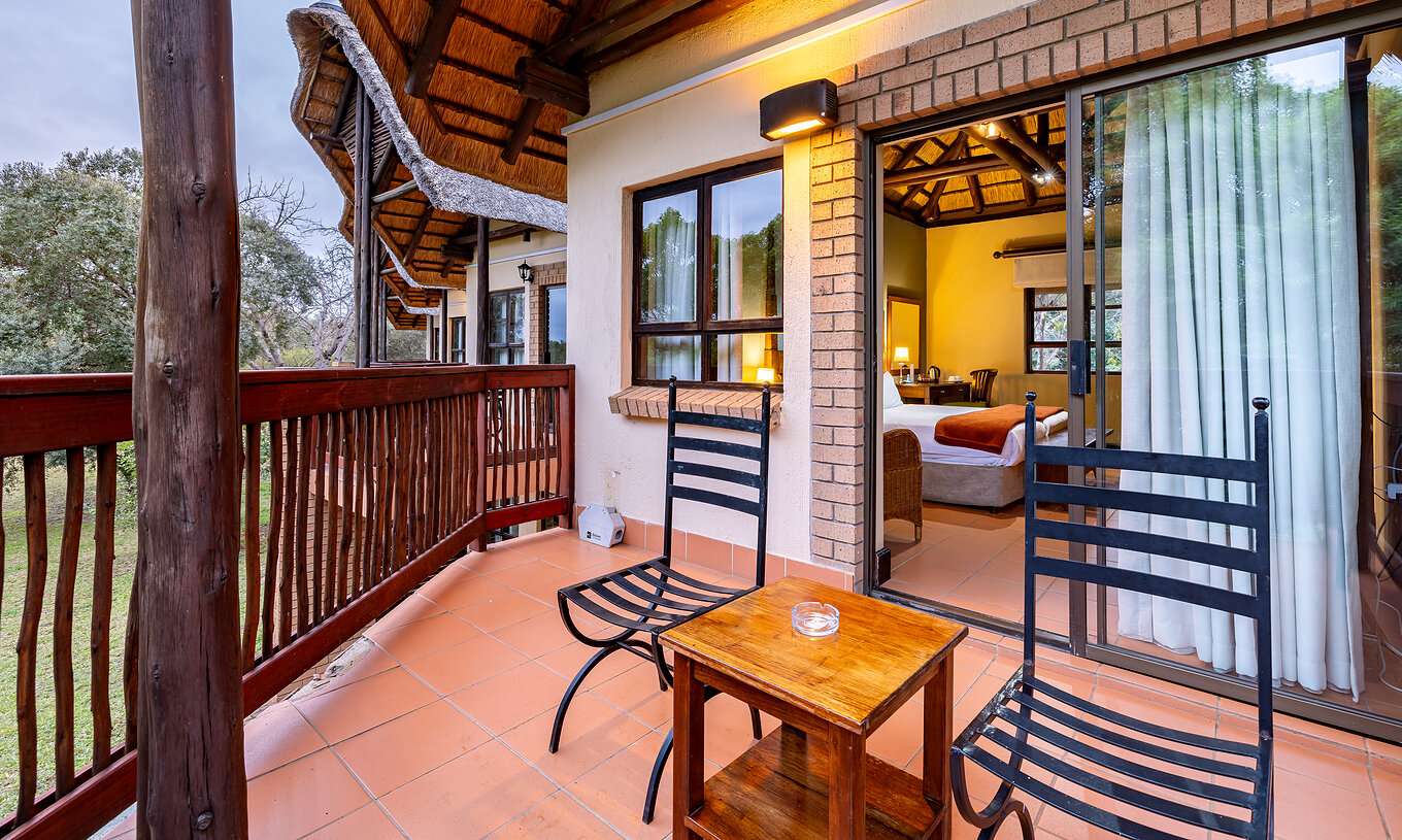 O Quarto Clássico do Pestana Kruger Lodge tem uma varanda com detalhes em madeira, duas cadeiras e uma mesa de apoio