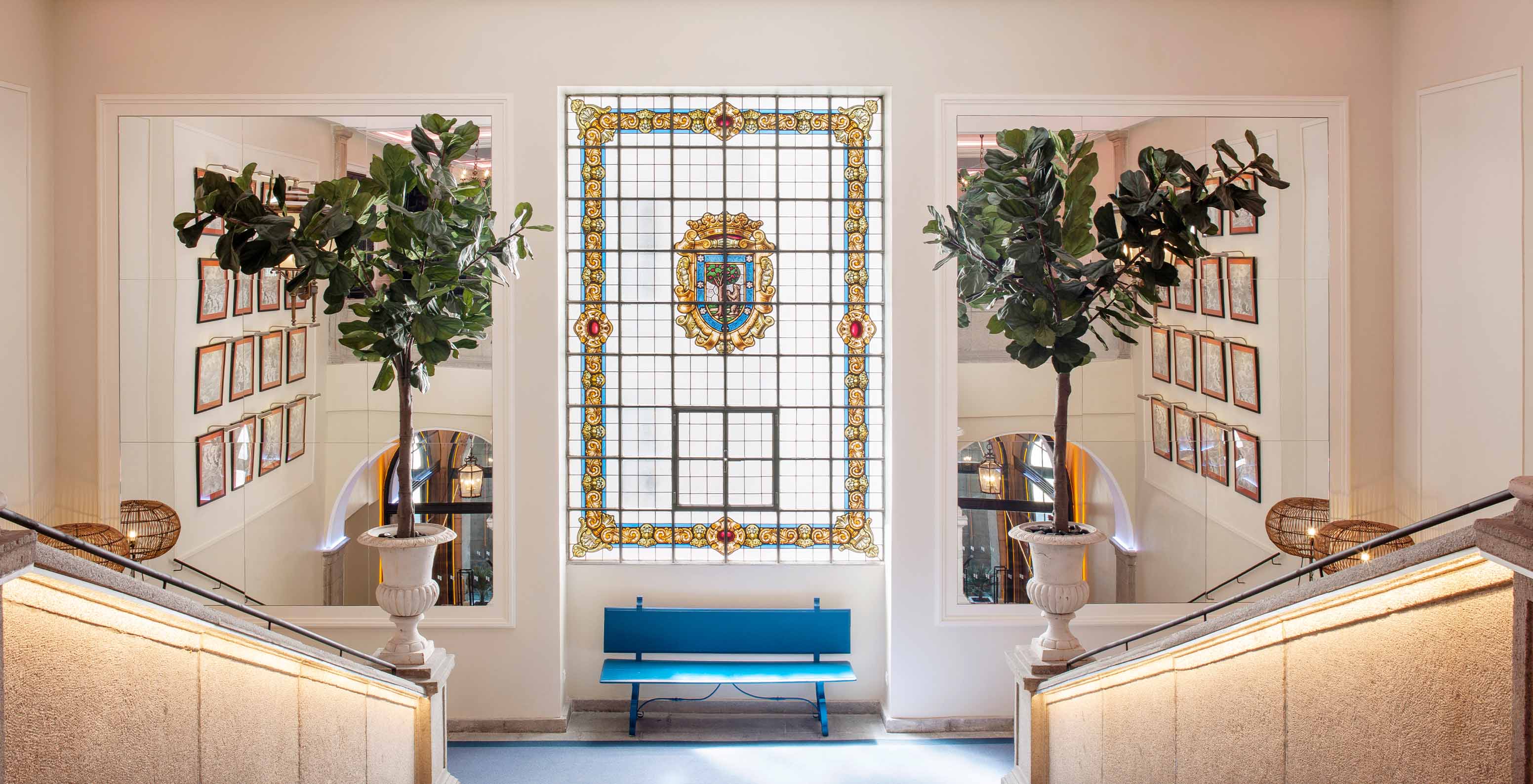 Escadaria interior do Hotel com Piscina na Plaza Mayor, em Madrid, com um vitral colorido ao fundo e dois vasos com árvores