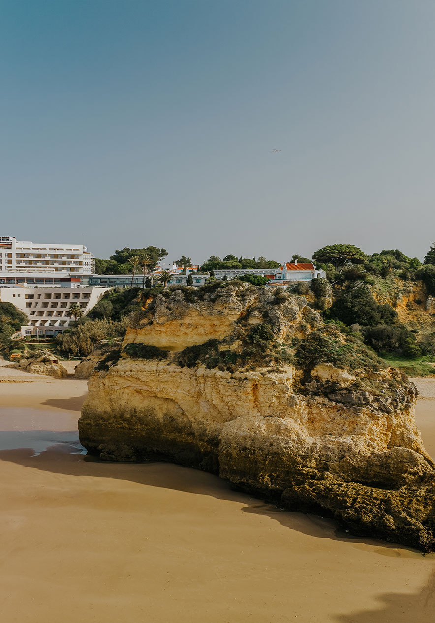 Praia do Alvor met rotsen, zand, vegetatie, de klif en gebouwen op de achtergrond, onder een heldere lucht