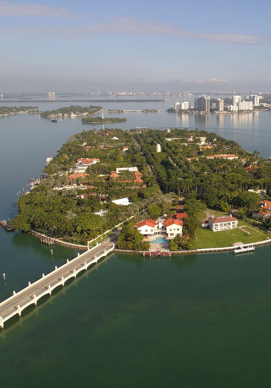 Luchtzicht op Star Island in Miami, met luxe huizen en dichte vegetatie, met een brug naar de stad
