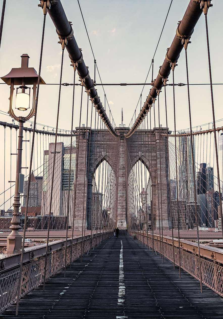 Panoramisch uitzicht op de Brooklyn Bridge, met stalen kabels en een ijzeren structuur onder een heldere blauwe lucht