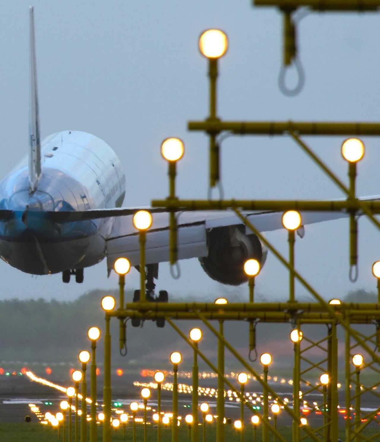 View of a large commercial plane landing on a lit runway with various lights at an airport