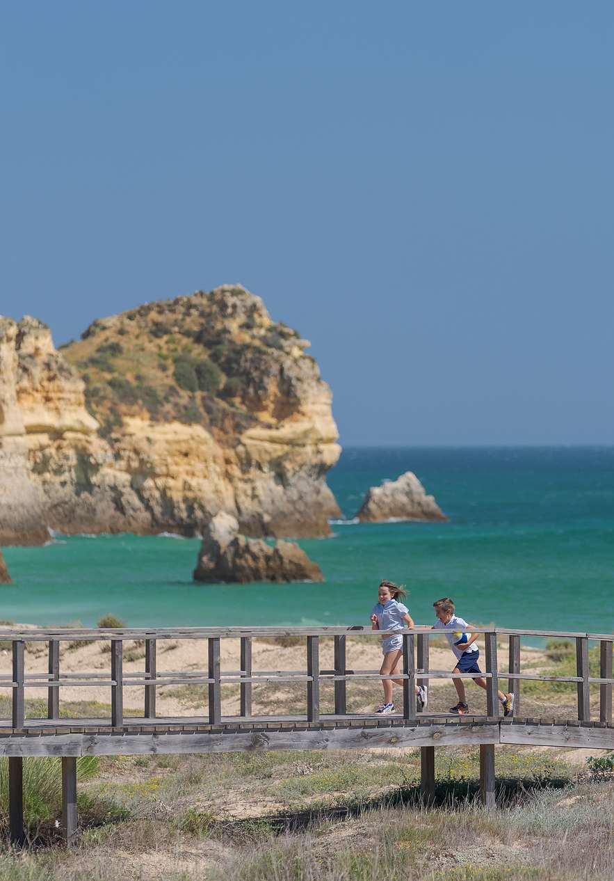 Parents and two children walking on a wooden boardwalk with views of the light blue sea and cliffs in the background