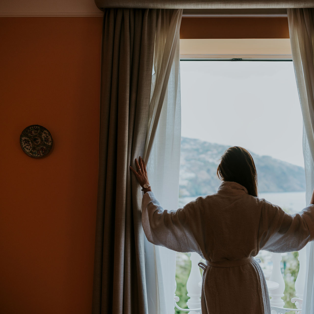 Woman in a robe enjoying the sea view from the window of a hotel in Madeira near the beach, with a pool