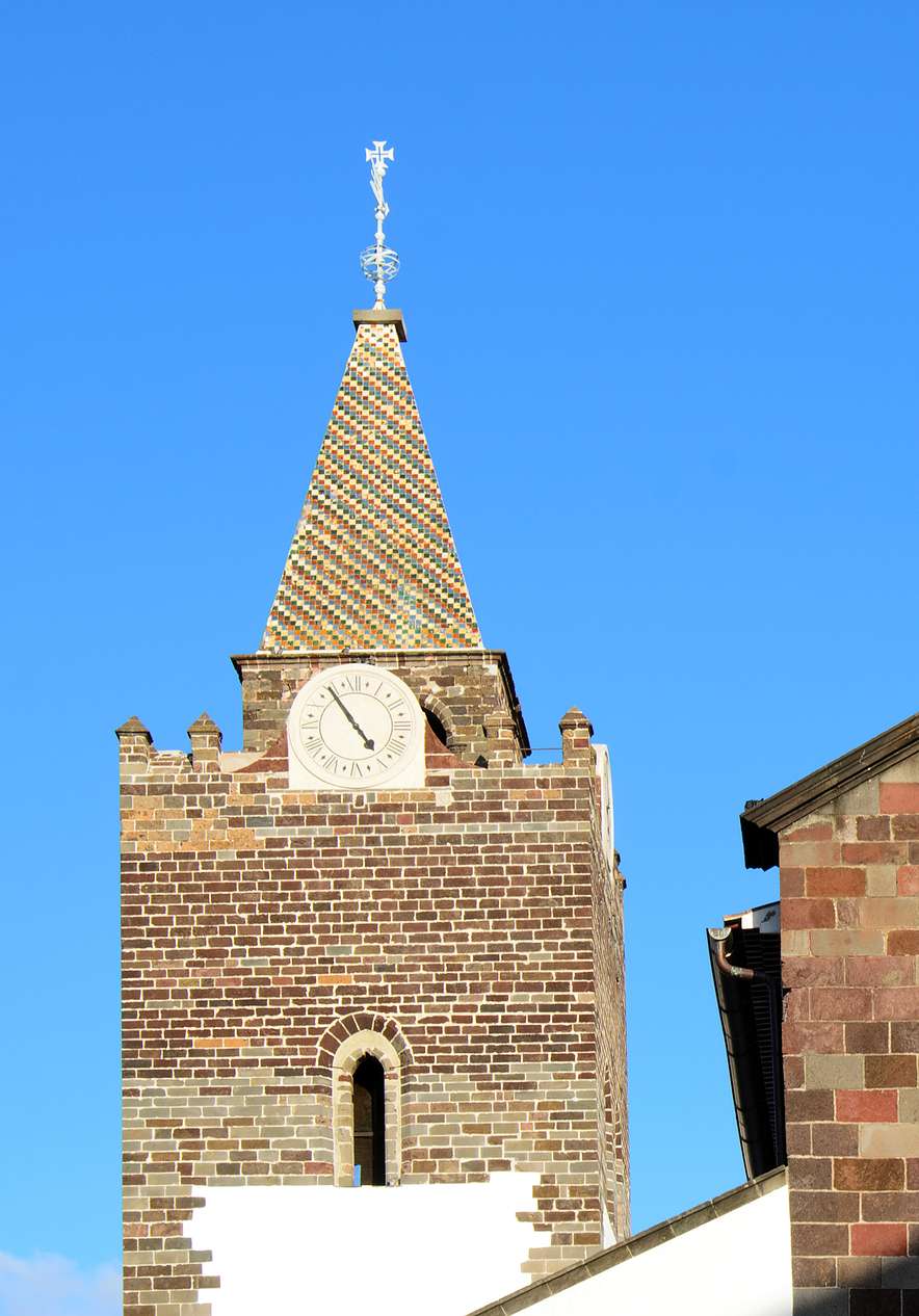 Funchal Cathedral with bell tower clock and stone facade under a blue sky