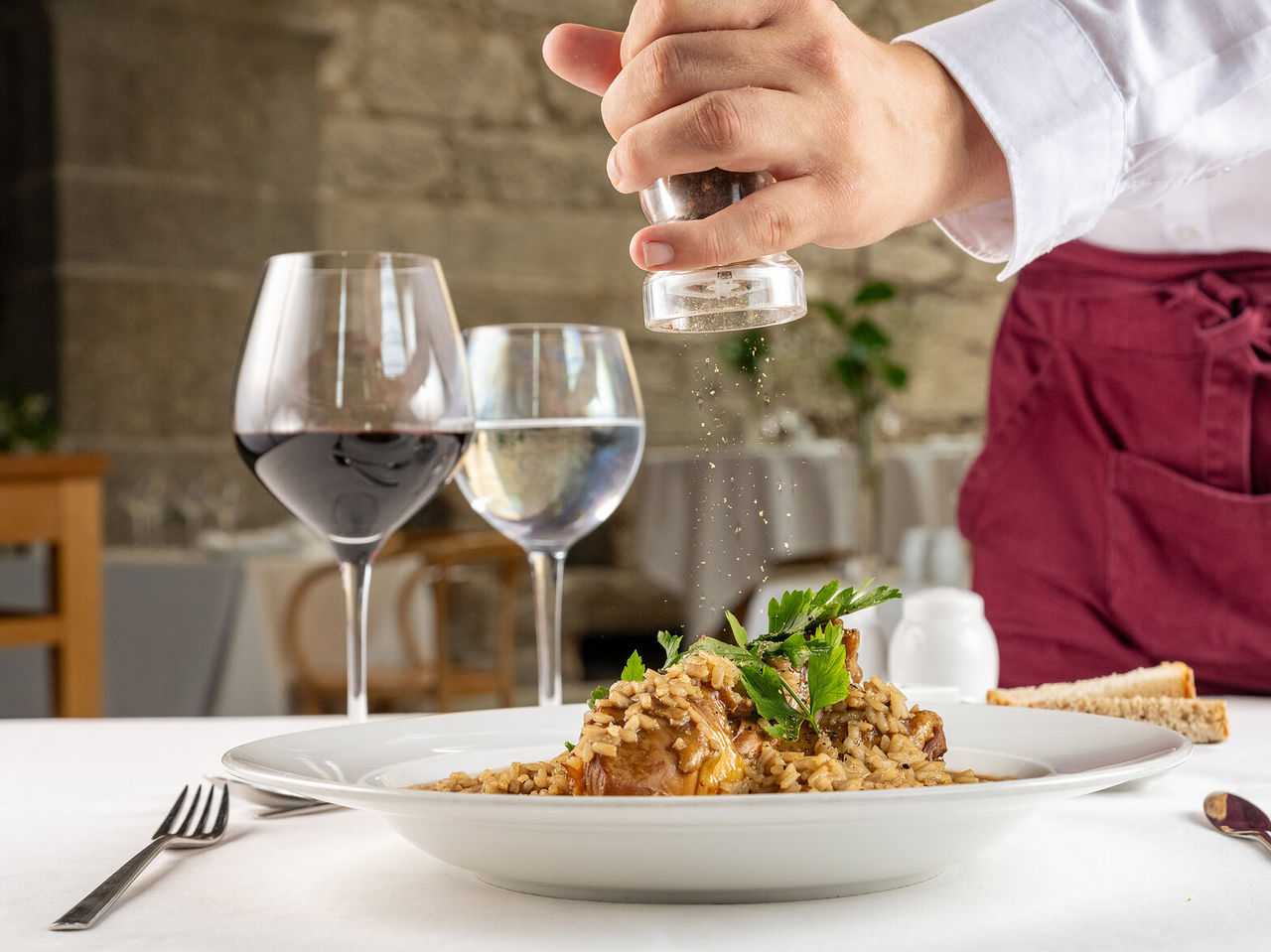 Plate of rice with meat, being seasoned with ground pepper by a waiter, accompanied by a glass of wine