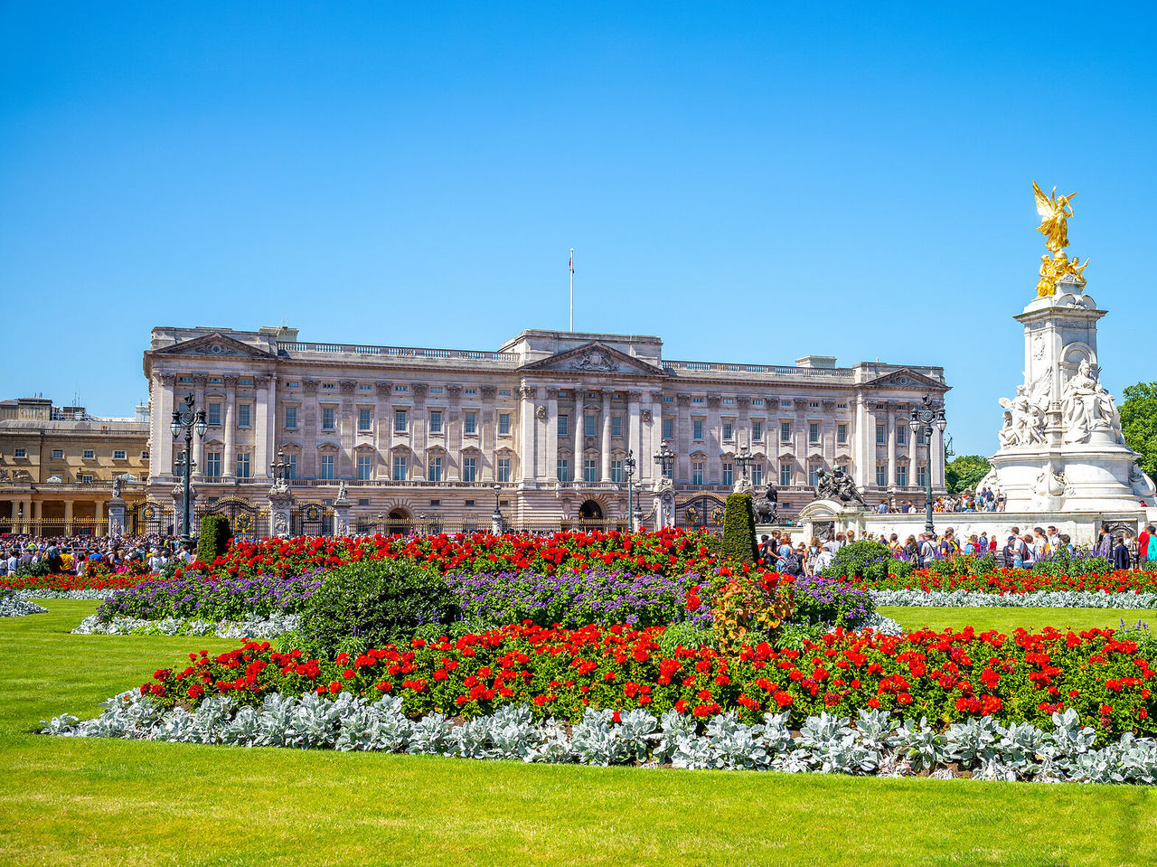 The imposing facade of Buckingham Palace in London, with a golden statue and a flower garden in front