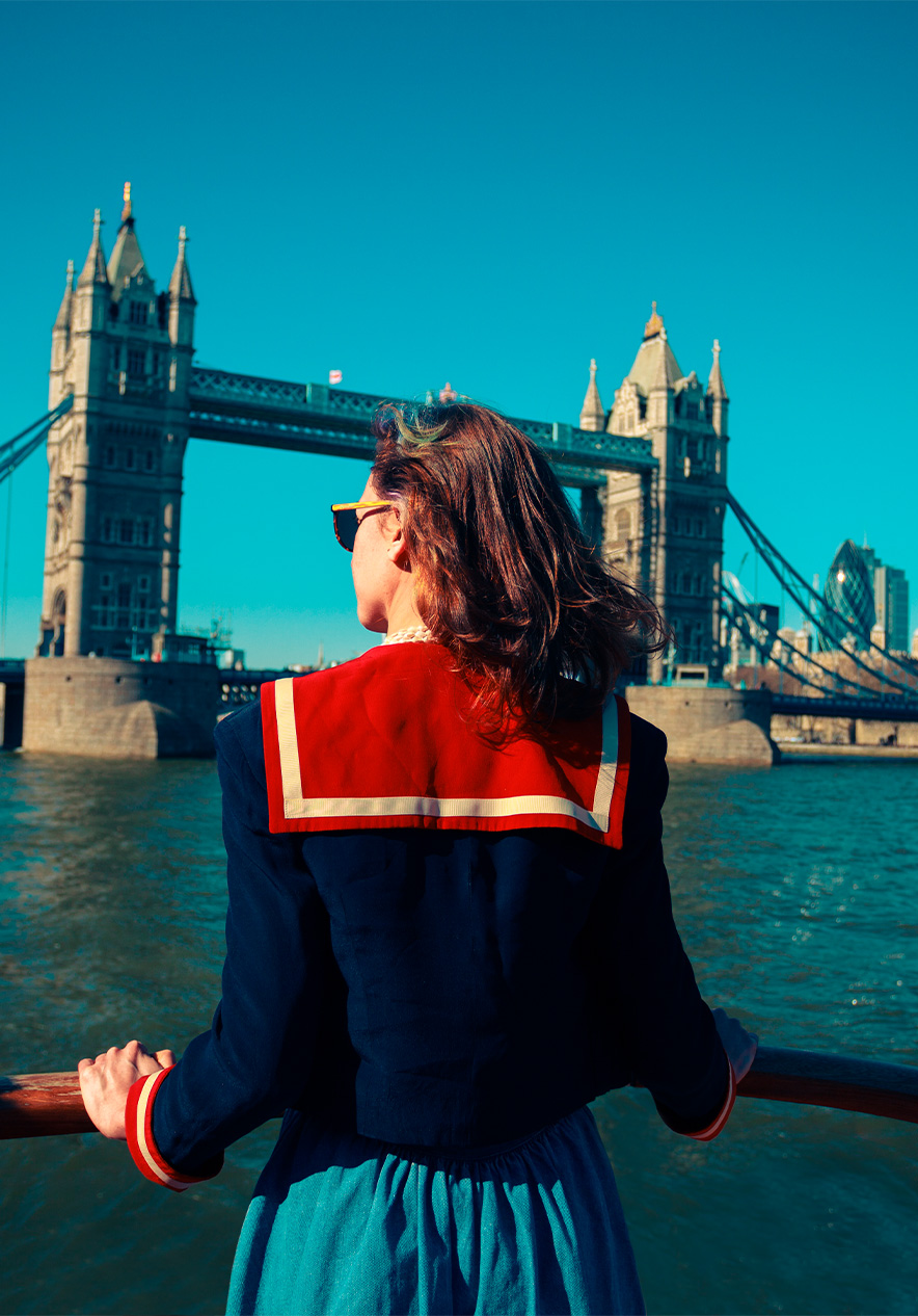 Boat ride on the Thames River with a lady at the front of the boat facing Tower Bridge under a clear sky