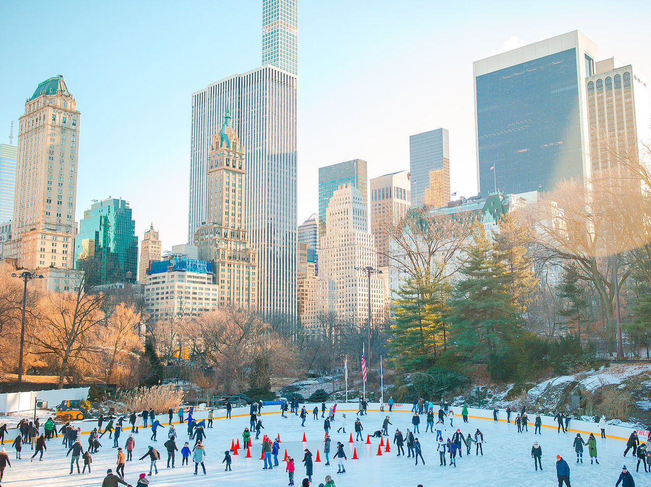 Bridge in a New York park covered in a layer of snow, with a frozen lake below and buildings in the background